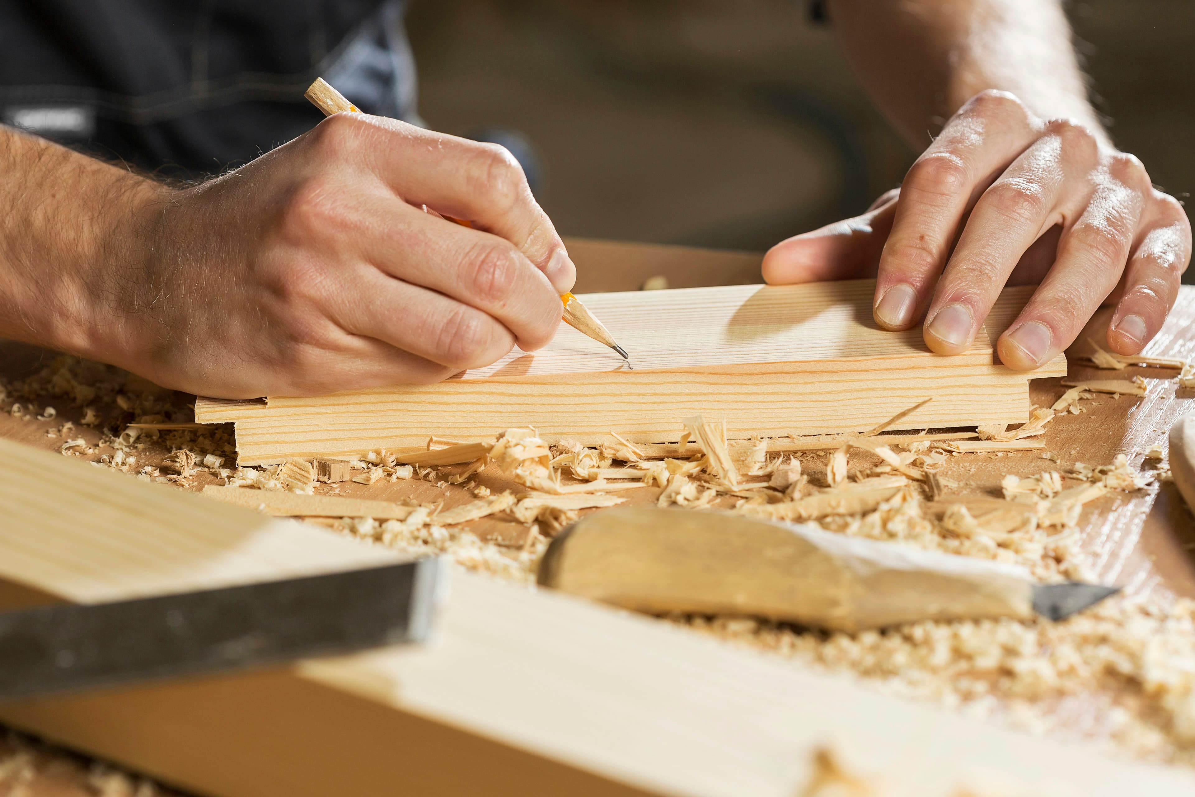 Hände zeichnen ein Maß auf einem Holzwerkstück an